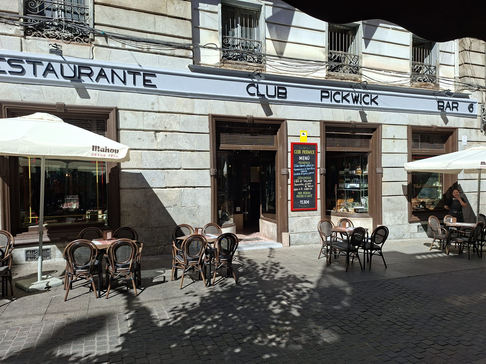 Fachada del restaurante iluminada con carpintería negra y jardineras.
